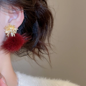 Close-up of a gold fireworks-shaped earring with a red pompom on a female model