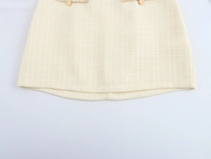 Détail de la mini-jupe en tweed beige avec texture tissée et boutons dorés décoratifs
