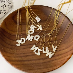Détail macro d'un collier doré avec des pendentifs en nacre naturelle et lettres d'alphabet