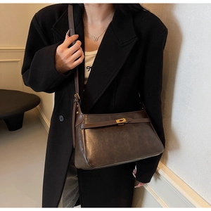 Borsa a tracolla vintage marrone scuro con chiusura a scatto dorata su cappotto nero