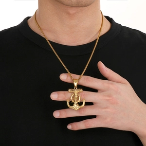 Detailansicht eines goldfarbenen Anker-Kreuz-Anhängers getragen auf schwarzem T-Shirt