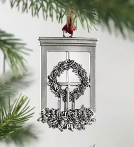 Detail of silver Christmas ornament with candle carvings hanging on a green pine branch