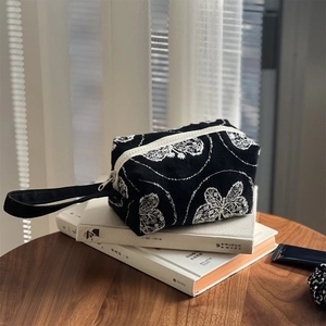 Detailed view of a black canvas bag with white floral embroidery on vintage books