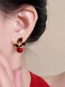 Close-up of retro flower earrings with deep red petals and crystal center on ear