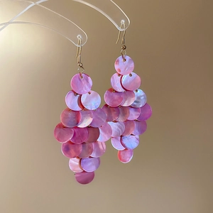 Detail von irisierenden rosa-violetten Muschel-Ohrringen mit goldenen Haken am Ständer