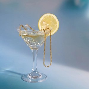 Collier minimaliste en acier plaqué or 18 carats posé sur un verre à cocktail glacé