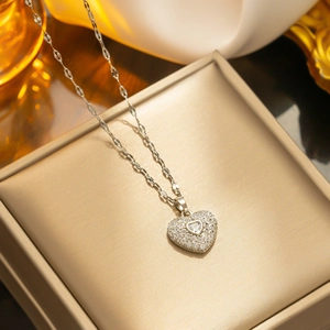 Silver titanium steel heart necklace with clear crystals on a gold jewelry box lid