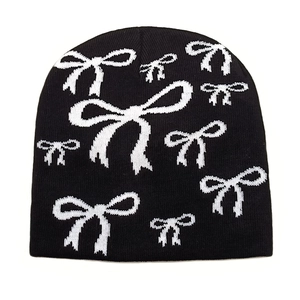 Close-up of black knitted beanie featuring white bow pattern and soft texture