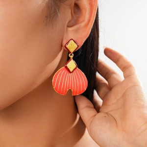 Detail of vintage red enamel shell earrings worn by a model on a clean white background
