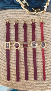 Flat lay of five vintage gold watches with burgundy leather straps on a woven mat background