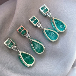 Detail of emerald green pear-cut drop earrings with silver finish on grey background