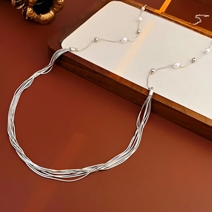 Macro detail of multi-layer silver chain necklace with faux pearls and long tassels