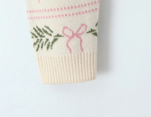 Detail of ribbed cuff and pink bow jacquard pattern on cream knit sweater