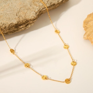 Hammered 18K gold disc necklace in stainless steel displayed on natural stones