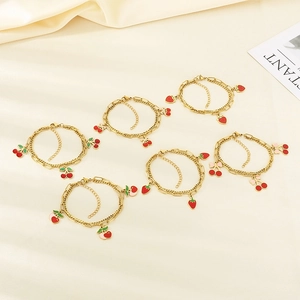 Detail of gold double-layered bracelets featuring red strawberry and cherry charms