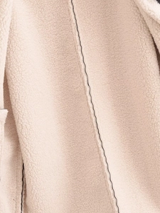 Close-up of beige faux shearling fabric with decorative black piping and soft texture