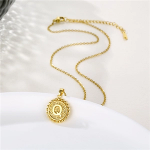 Close-up of gold pendant necklace with letter Q engraving and beaded edge detail