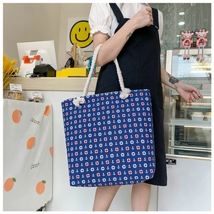 Blue canvas tote bag with nautical anchor pattern and thick white rope handles on shoulder