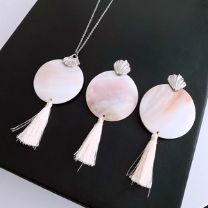 Detailed close-up of shell pendant necklaces with cream tassels on black surface