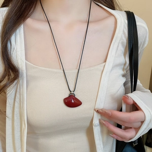 Close-up of a minimalist necklace with a dark red irregular pendant on a black cord