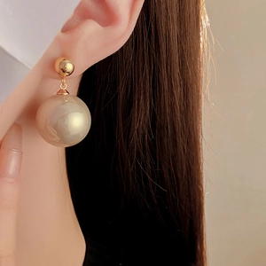 Detail of large pearl drop earrings on a model showing elegant gold and white jewelry style