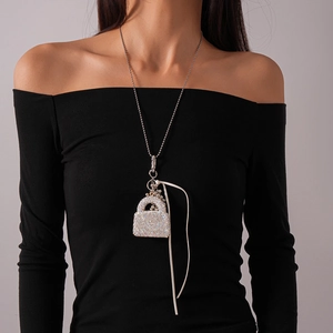 Détail du collier pull à perles argentées avec pendentif sac en strass et cordon en cuir blanc