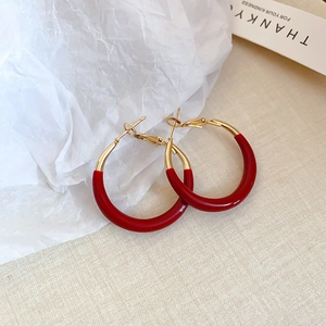 Detail view of retro red and gold hoop earrings on textured beige fabric background