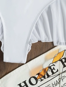 Macro detail of white bikini bottom featuring mesh ruffle trim on warm wood background