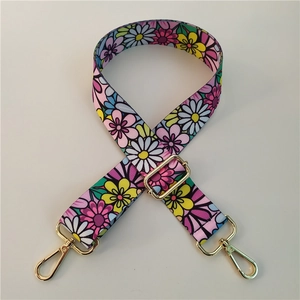 Macro view of adjustable floral wide bag strap with gold metal hooks and daisy pattern