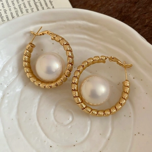 Macro shot of gold-plated twisted hoop earrings with white round pearls in a ceramic tray
