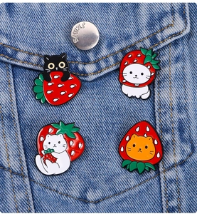 Close-up of four cute cat strawberry enamel pins displayed on a denim jacket pocket