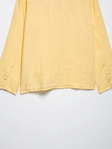 Detail view of yellow linen shirt hem and sleeve cuff with natural fabric texture