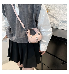 Pink crescent handbag with silver metal studs worn by model in casual style