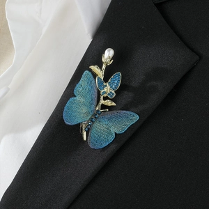 Elegant gold butterfly brooch with blue gradient wings and pearl detail on black suit