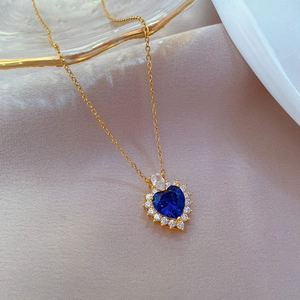 Macro shot of gold heart necklace featuring a blue gemstone and pavé crystal border