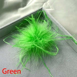 Detailed close-up of lush green ostrich feather brooch on grey velvet jewelry tray
