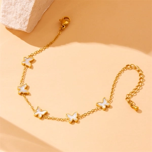 Elegant gold chain bracelet featuring white butterfly shell pendants on a peach background