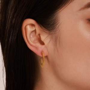 Golden C-shaped sunburst hoop earrings with textured beads on female model