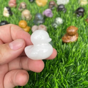 Handheld carved white crystal duck gemstone figurine with blurred garden background