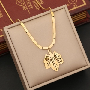 Close-up of golden leaf pendant on a stainless steel box chain over a beige jewelry box