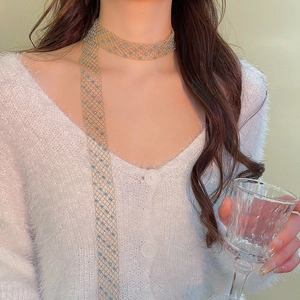Detail of a gold mesh choker with light blue crystals worn by a model on a soft background