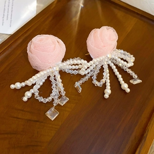 Detail view of pink fabric rose earrings with white pearls and crystal tassels displayed on wood