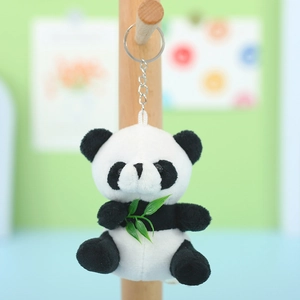 Plush panda keychain holding a green bamboo leaf with metal ring on a wooden stand