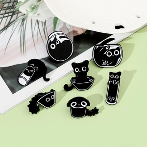 Flat lay of seven cartoon black cat enamel pins in various poses on green background