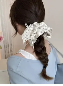 Detailed back view of a polka dot silk bow scrunchie on a thick braided hairstyle