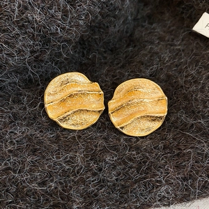 Vue macro de boucles d'oreilles dorées avec texture froissée sur fond de tricot gris