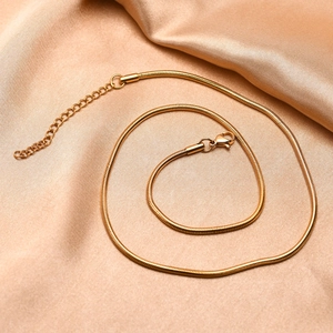 Detail of golden stainless steel snake chain necklace on silk champagne fabric backdrop