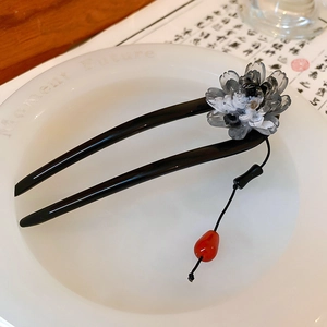 Detail of a U-shaped wooden hairpin with black floral petals and a red teardrop charm