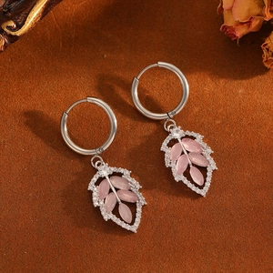Detail of silver leaf hoop earrings with pink gemstones and zircon accents on a rustic base