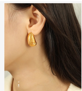 Detail of model wearing gold-plated spiral horn earrings with vintage metal texture